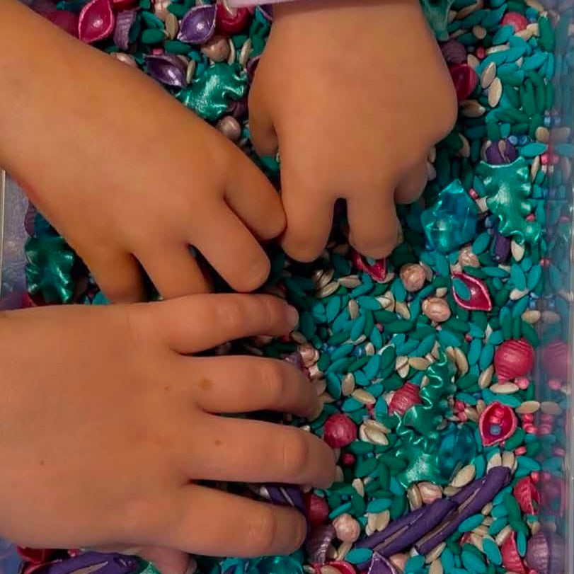 Children's hands interacting with colorful sensory materials in a clear container